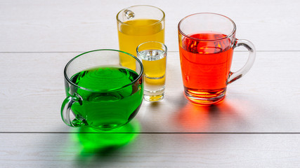 Three carbonated drinks green, yellow, red in different shaped glass mugs and a glass of pure water on a wooden table