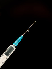 a syringe with a vaccine and a needle. Liquid drips from the needle