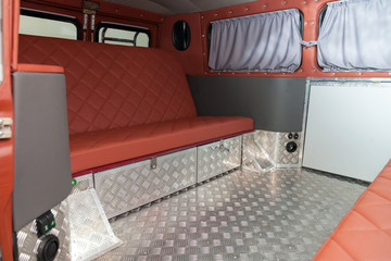 The interior of the car in the back of a van converted into a motor home for off-road and travel with a brown leather interior, a folding table and aluminum floor trim.