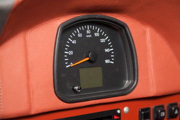 Simple analog car speedometer with a red arrow on a leather trimmed panel.