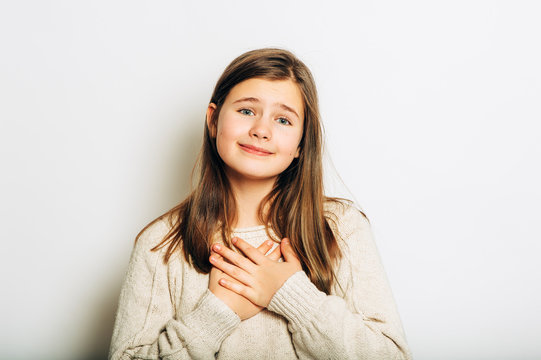 Studio Portrait Of Thankfull Young Girl With Happy Facial Expression, Holding Hands On Chest