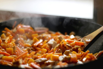 Stir frying carrot, red kuri squash and portobello mushrooms. Selective focus.