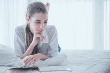 Young woman enjoying reading a book while lay down on the bed.