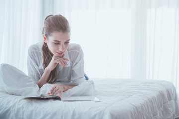 Young woman reading on the book at her bed.