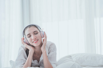 Young woman listening to music with earphones lying down on the bed.