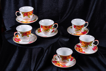Set of cups and saucers for tea and coffee on a dark black fabric background