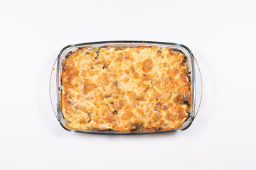 Baked salmon with potatoes under a cheese brown crust in a glass pan on a white background