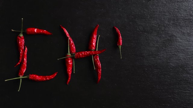 Stop motion animation of red hot peppers writing chili on slate background
