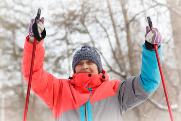 elderly woman in a winter park holding ski poles in her hands. Winter sport. Activity of retirees.