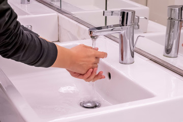 Young girl is washing her hands under pouring water from tap in water closet room with mirror. Concept of self hygiene and cleanliness