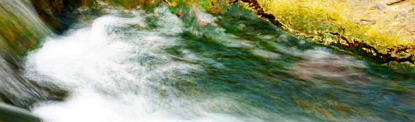 panoramic view of a small stream on algae background in the early spring day. waterfall in the forest. 