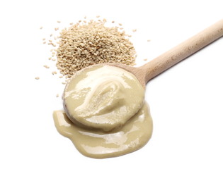 Nut butter or sesame paste tahini in wooden spoon and organic integral sesame seeds isolated on white background