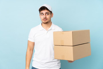 Delivery caucasian man isolated on blue background standing and looking to the side