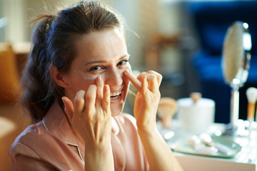 woman at modern home in sunny winter day applying eye cream
