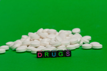White round pills on a green background and the inscription drugs on black cubes