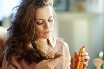 concerned woman holding hair oil bottle and checking hair ends