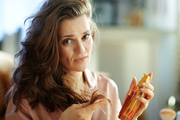 sad modern woman holding hair oil bottle and checking hair ends