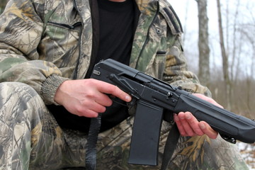 Man in protective clothing with automatic firearm hunting weapons in the forest