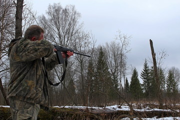 Man in protective clothing with automatic firearm hunting weapons in the forest