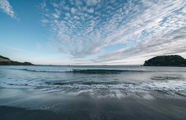 Opposing patterns of clouds in sky and backwash of waves on sand.