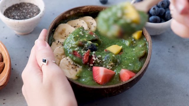 Eating raw green smoothie bowl with superfoods. Healthy lifestyle, clean eating concept. Female hands taking spoonful of detox green spinach smoothie