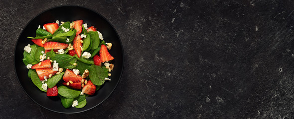 Top view of healthy strawberry spinach salad on black background