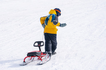 Back view of child in pulling sledge and running up snowy slope