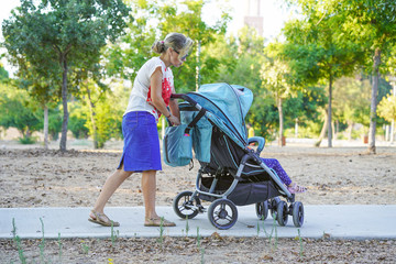 Young mom with baby carriage. Woman with a baby carriage for two children walks in the park on a summer morning. Walking. Back view.