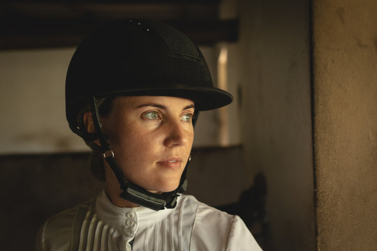Caucasian woman with helmet standing inside a dressage horse stable