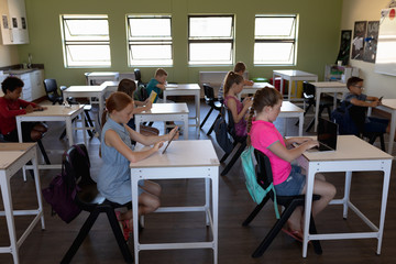 Group of schoolchildren sitting at desks using personal computers