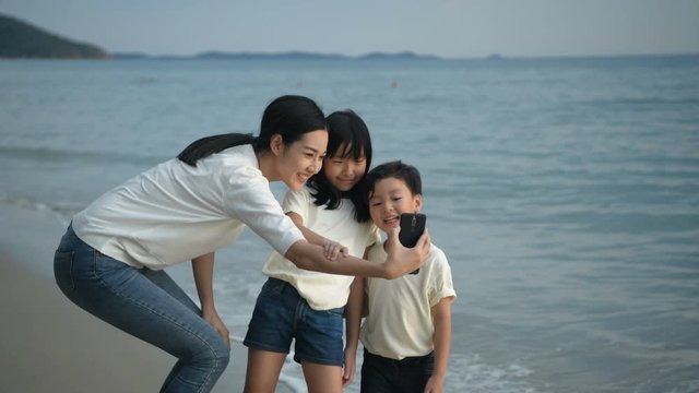 Holiday concept. Mother and children are taking pictures together on the beach. 4k Resolution.