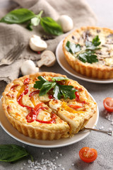 The concept of French cuisine. Quiche with peppers, tomatoes and mushrooms on a light background. Background image, copy space