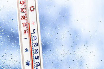 A thermometer against a glass window with rain drops shows 15 degrees of heat. Rainy weather_
