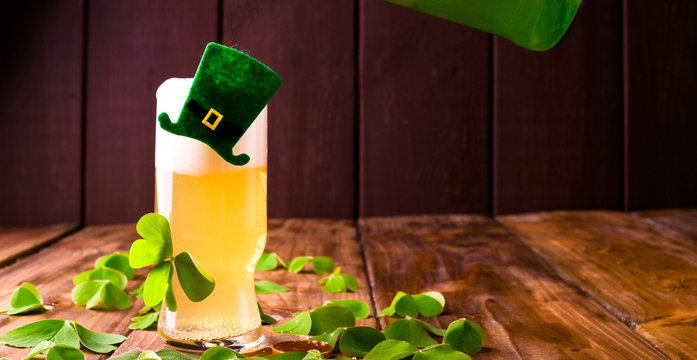 A glass of frothy beer with decor and fresh clover leaves. Drink on a wooden background. Concept of images for the traditional holiday of St. Patrick's Day. Copy space.
