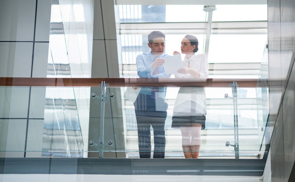 Business Colleagues Meeting In Modern Office Space Stock Photo. Male And Female Professionals Are Planning Strategy In Brightly Lit Workplace. They Are Seen Through Glass Wall With Reflections.