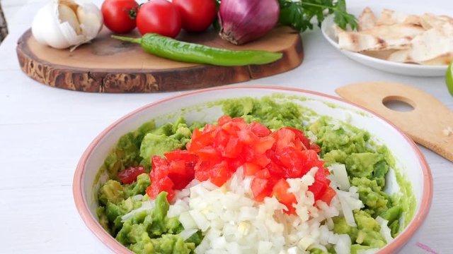 Chef presses garlic with a galic press and adds it to a bowl of guacamole ingredients. Recepy for avocado spread