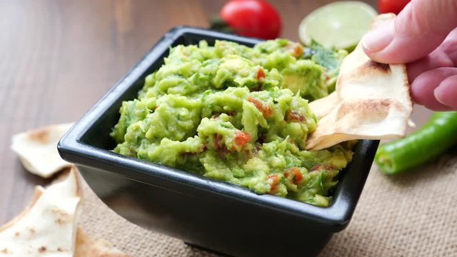 Hand dipping a nacho chip into a bowl of freshly made guacamole