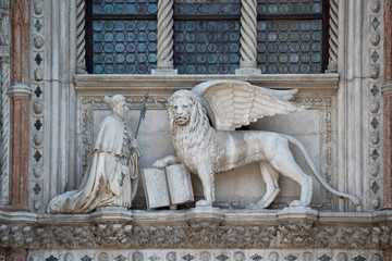 Winged Lion and a priest with a Bible at St. Mark's Square, Doges Palace. Fragment of Palazzo Ducale entrance. The Lion is the symbol of Venice. Translation:"Peace be with thee, O Mark, my evangelist"
