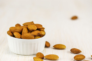 Almonds in a white bowl and on a white wooden surface