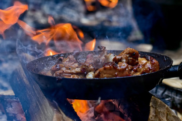 Juicy fried chicken in a smoked pan on a campfire