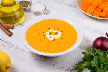 Pumpkin soup in a white plate with ingredients on a white wooden table. Selected focus