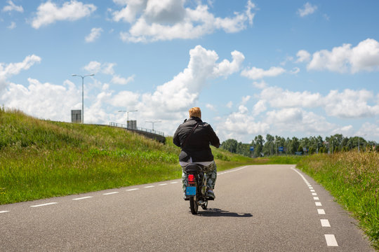 Woman on a asphalt road with a moped in the dutch village of Leiderdorp.