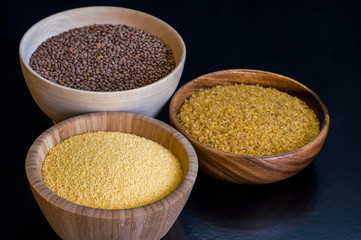 Cereals couscous, bulgur, red lentils in wooden bowls on a black background. Concept of Eastern cuisine dishes