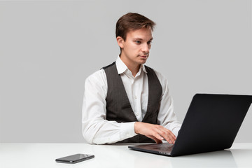 Businessman in a white t-shirt and grey vest working on a laptop. Man looking at the camera