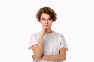 Thoughtful young woman in a white shirt and eyeglasses looking positively into a camera