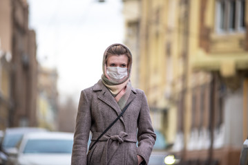 Fototapeta na wymiar Young attractive european caucasian woman in medical protective mask against influenza viruses and coronavirus COVID-19 on a city street