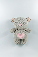 a small knitted toy grey bear cub with a pink heart on its belly
