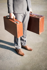 Unrecognizable businessman standing outdoors on the street waiting with weathered old brown luggage...