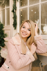 Christmas portrait of a girl in a pink dress and sheepskin coat on the background of the Christmas decor of the house in an elegant interior. A woman is preparing to celebrate Christmas and New year