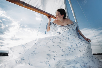 Нoung girl stands on a yacht with white sails in a flying dress.